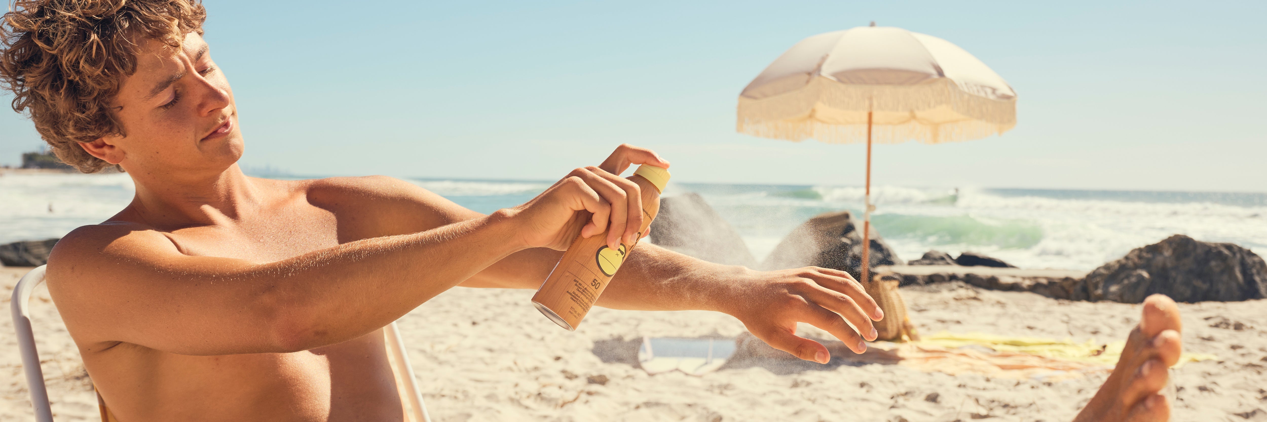 Man applying sunscreen spray on a beach