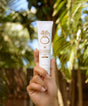 Hand holding a Sun Bum sunscreen tube with palm trees in the background