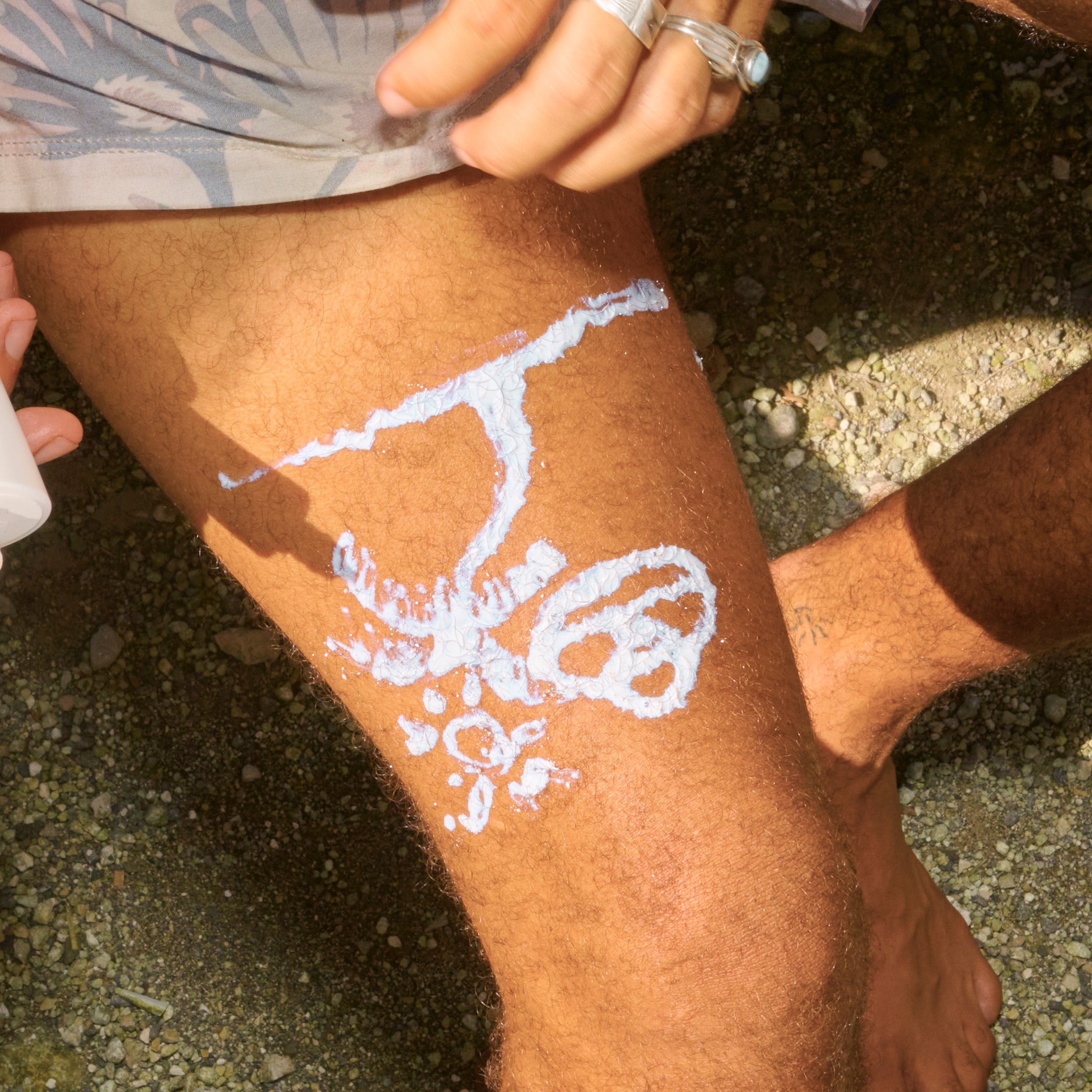 Person applying white cream or lotion to a leg outdoors