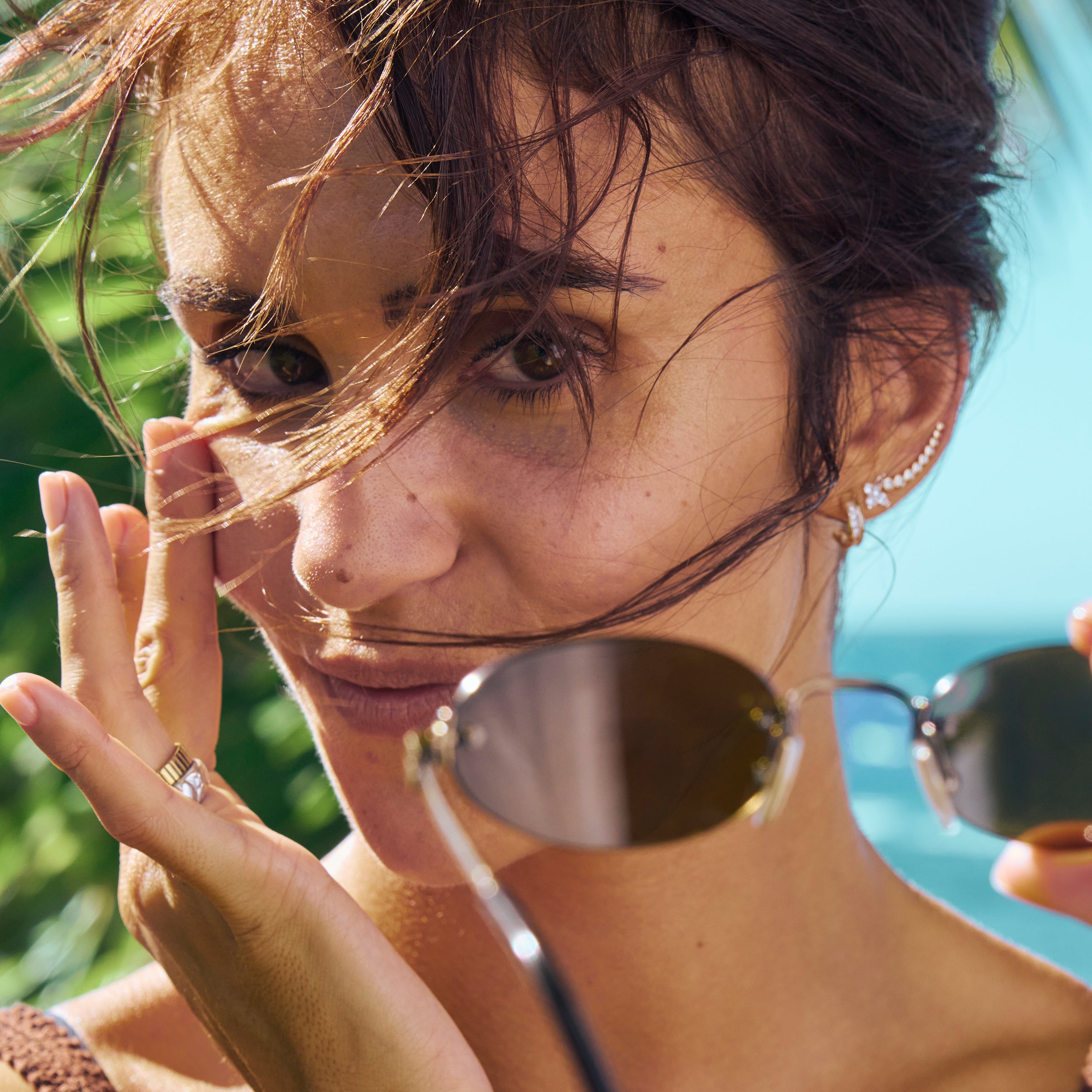 Woman with sunglasses and hair blowing in the wind by a beach