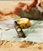 Sun Bum sunscreen bottle on a beach with bananas and a book