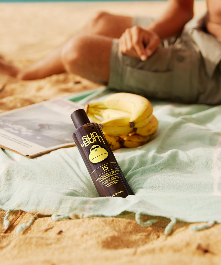 Sun Bum sunscreen bottle on a beach with bananas and a book