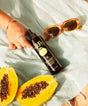 Sunscreen spray bottle, sunglasses, and papaya on a light fabric background