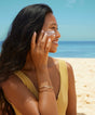 Woman applying sunscreen on a beach with clear blue sky and ocean in the background