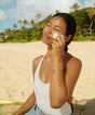 Woman applying sunscreen on a beach with palm trees in the background