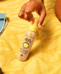 Hand holding a bottle of Sun Bum Leave In product on a yellow textured surface