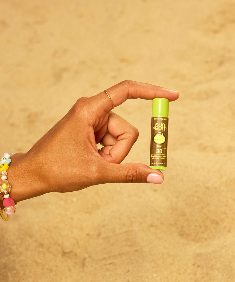 Hand holding a small green bottle with a beige background
