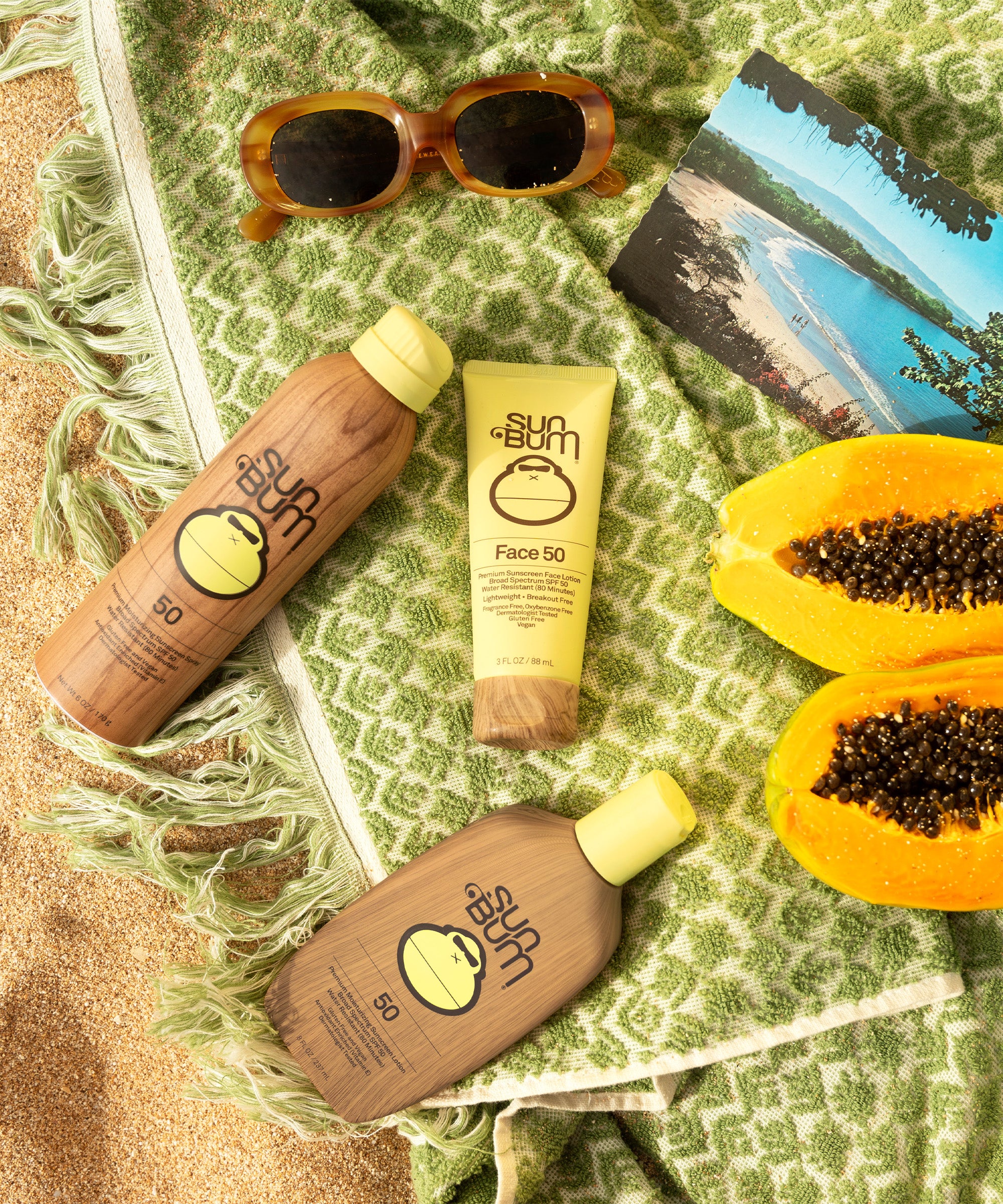 Sunscreen bottles, sunglasses, and a papaya on a green textured surface