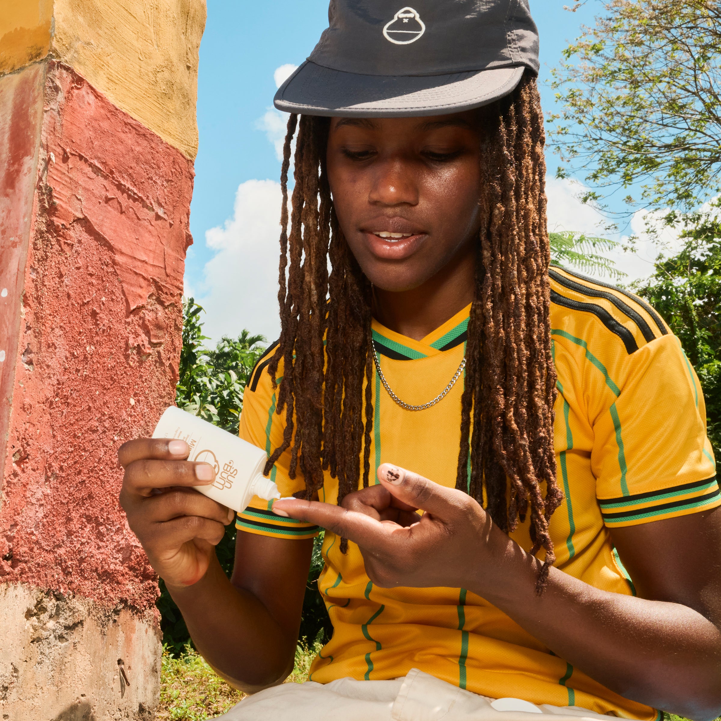 Person in yellow and green sports jersey with cap holding a snack outdoors