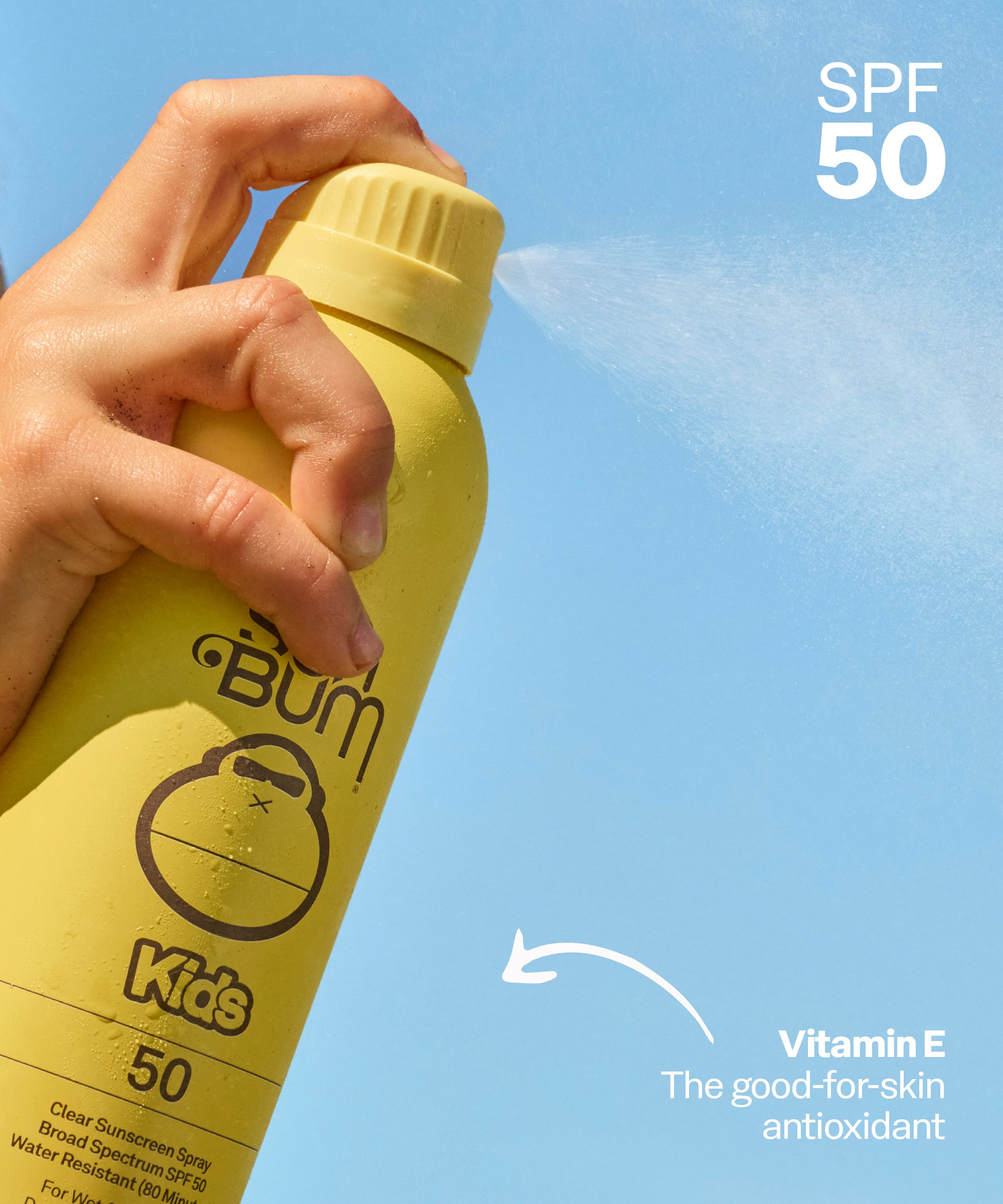 Yellow sunscreen spray bottle with 'Bum Kids' branding against a blue sky.