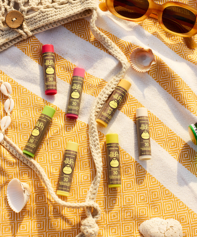 Sunscreen bottles on a yellow patterned towel with sunglasses and shell decorations.