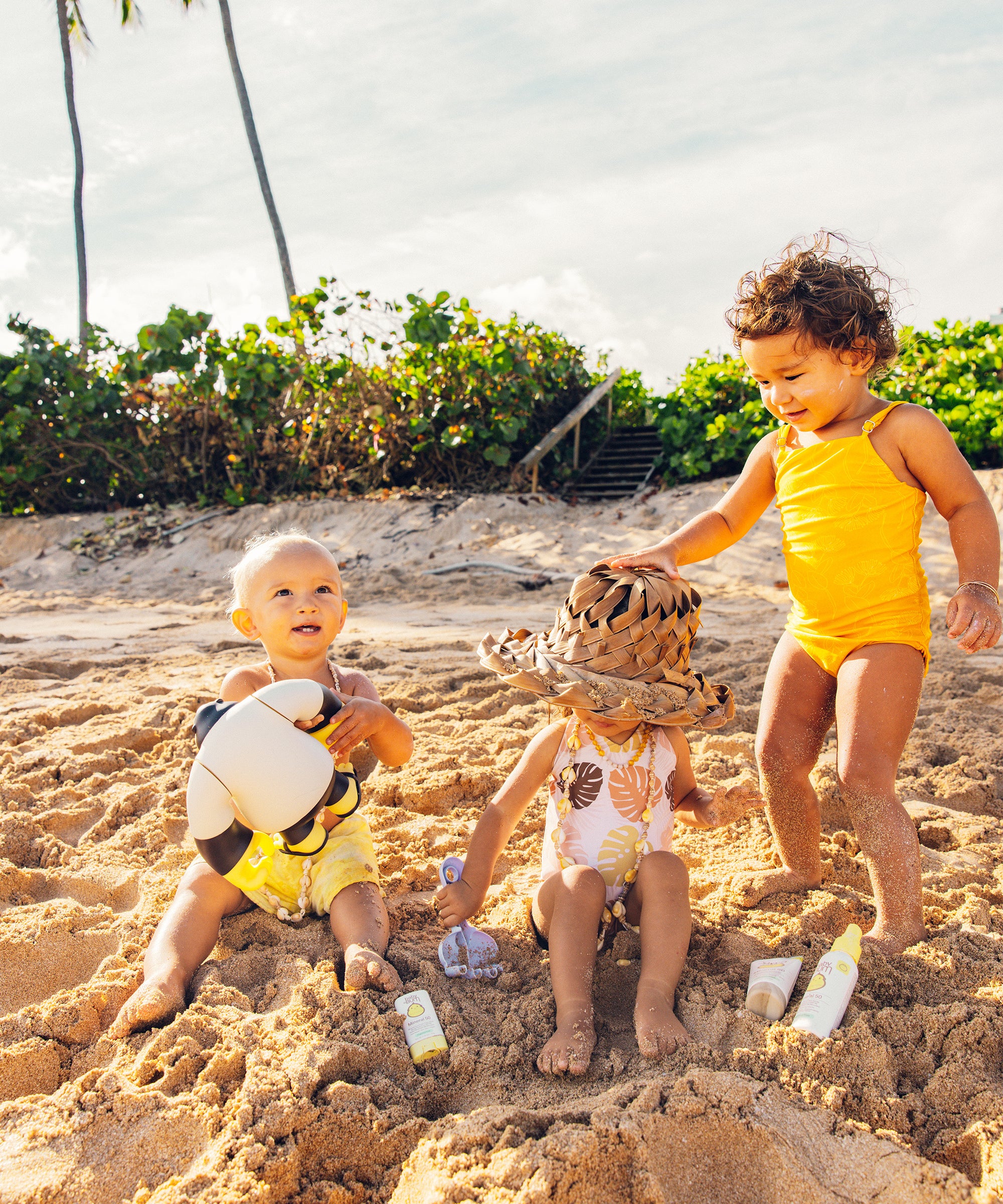 Three children playing in the sand on a beach with palm trees in the background.