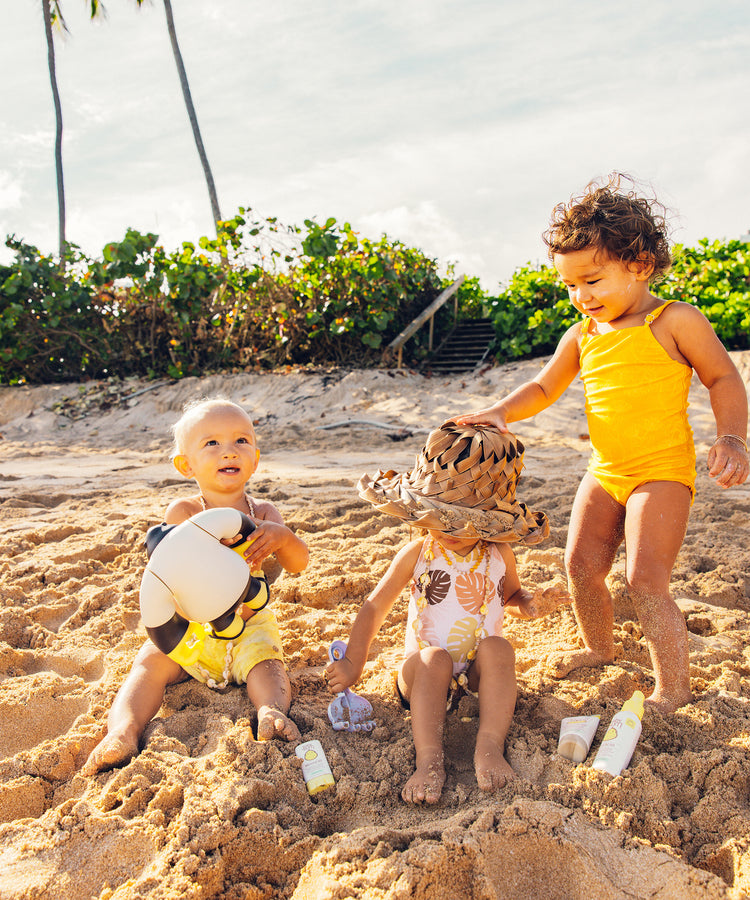 Three children playing in the sand on a beach with palm trees in the background.