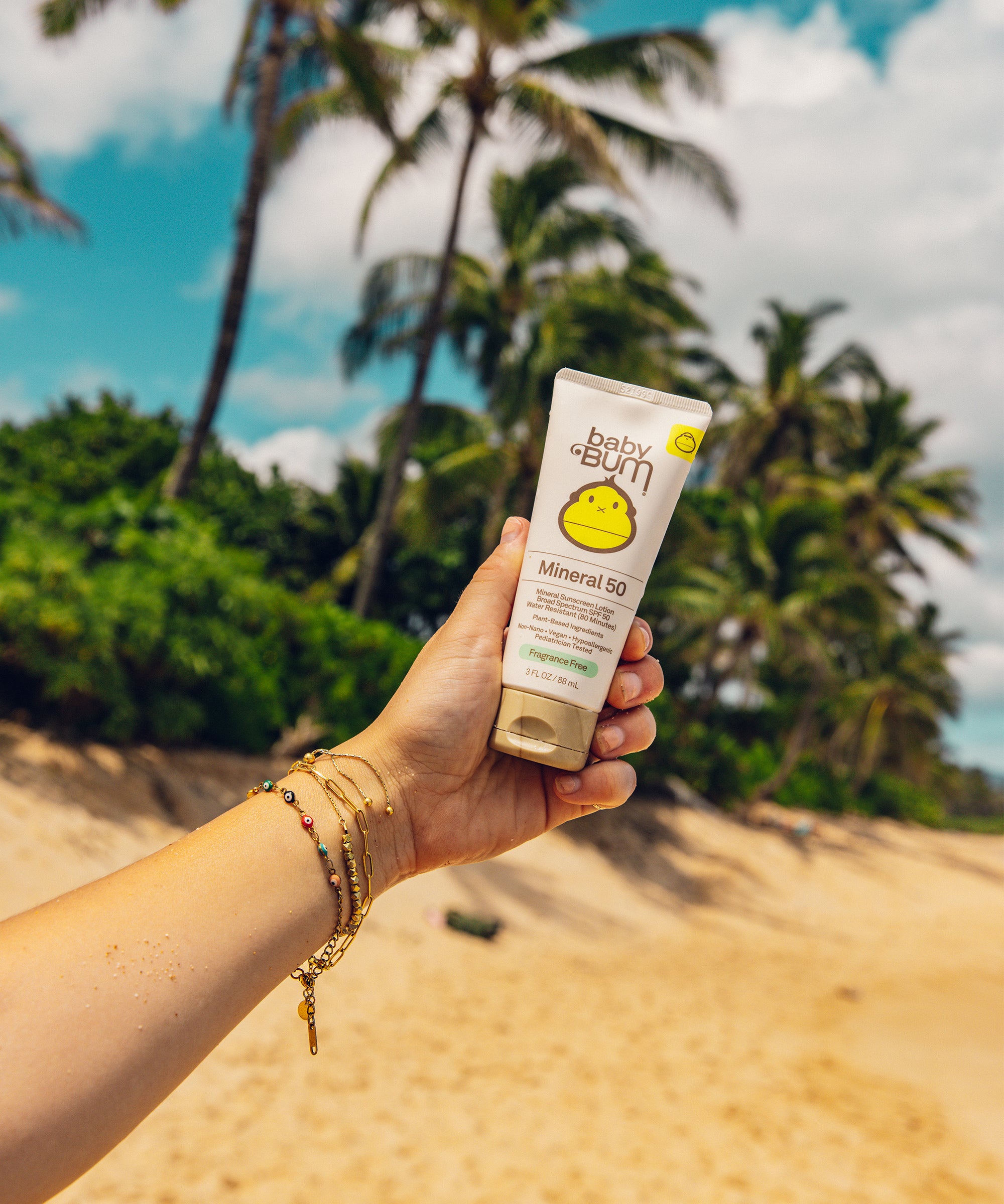 Hand holding a sunscreen bottle with palm trees and blue sky in the background