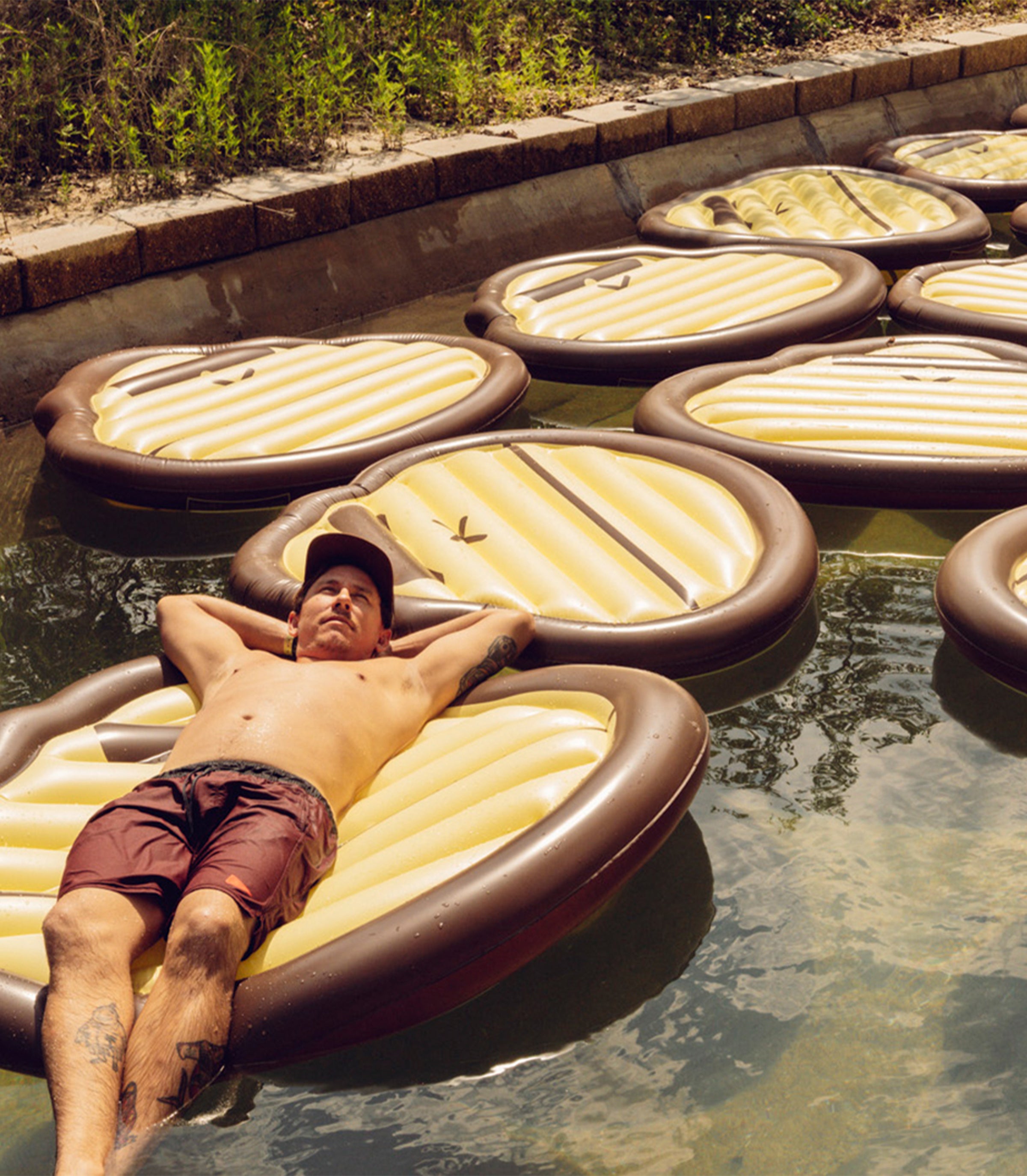 Man lying on an inflatable pool float in a pool with other similar floats.