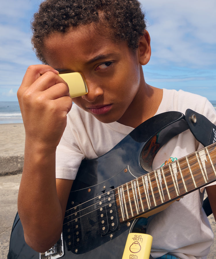 Child holding a guitar on a beach with a blue sky