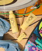 Sunscreen bottles and a tube on a wooden surface with sunglasses and denim jeans.