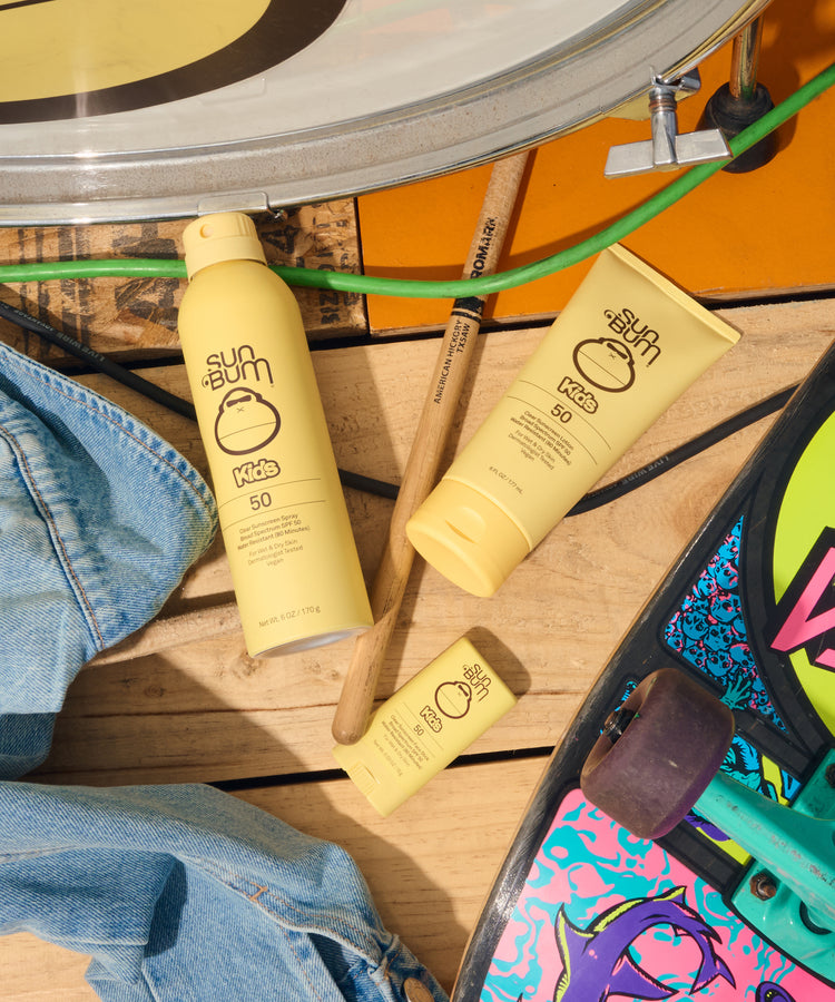 Sunscreen bottles and a tube on a wooden surface with sunglasses and denim jeans.