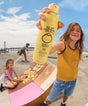 Child holding a Sun Bum Kids sunscreen bottle on a beach with another child in the background.