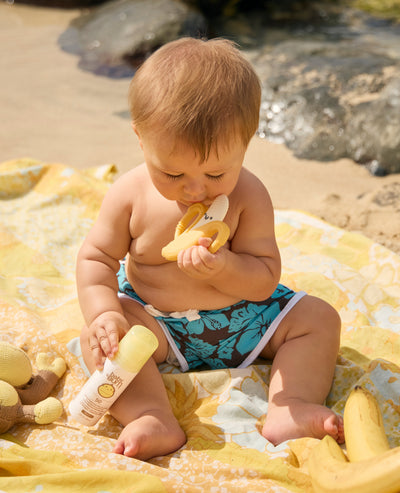 Baby playing with banana toys on a beach blanket
