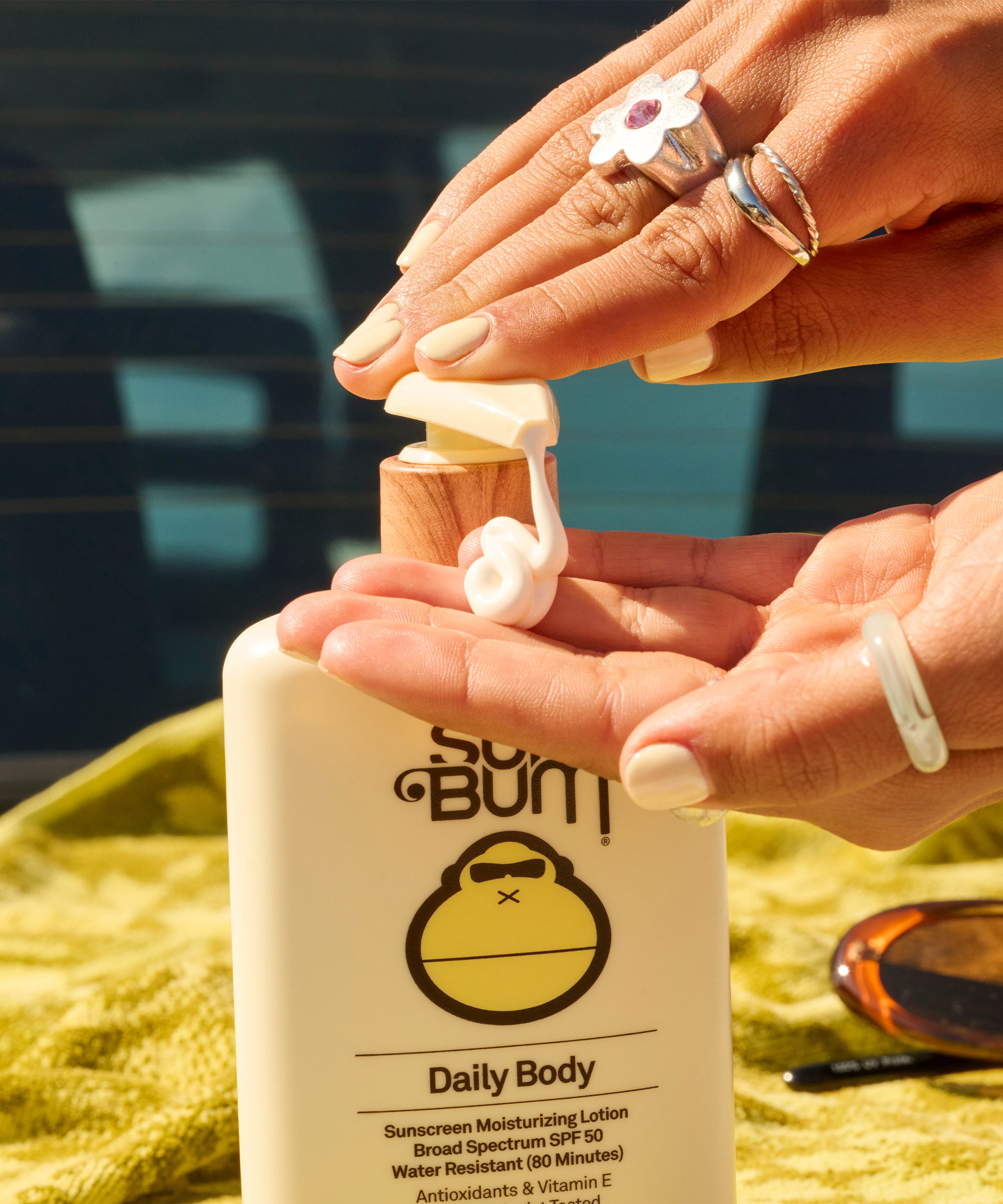 Person applying So Bum Daily Body sunscreen lotion on a blurred outdoor background