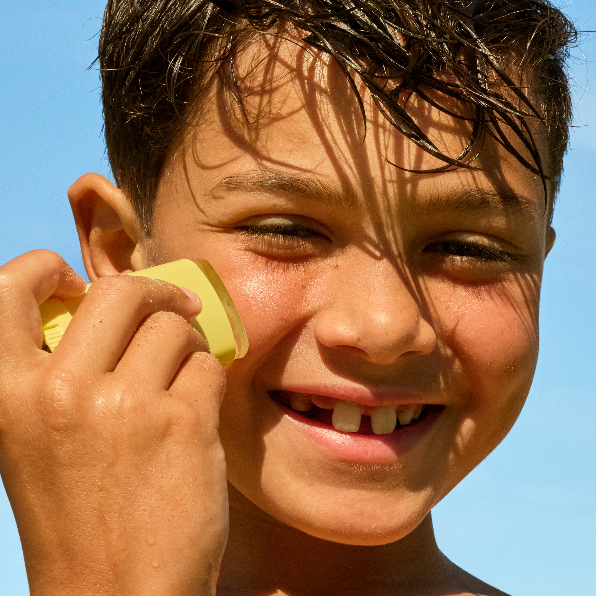Child holding a yellow object to their ear against a clear blue sky