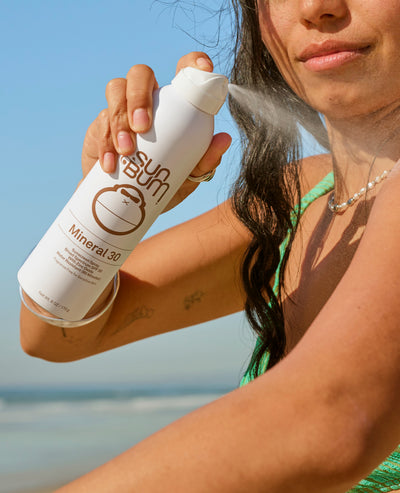 Person applying sunscreen spray on a beach