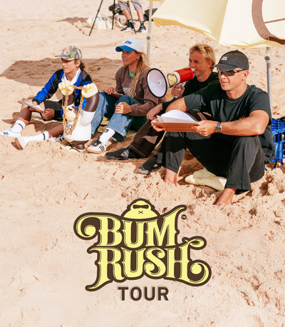 Group of people sitting on sand with 'Bum Rush Tour' logo