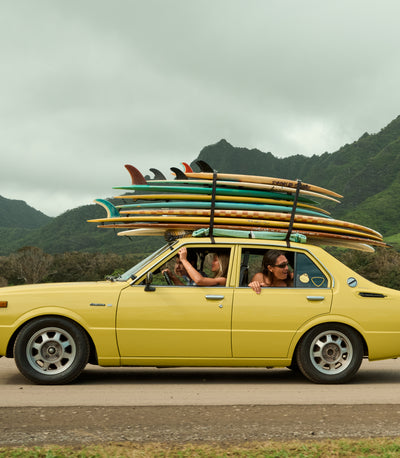 Yellow car with surfboards on top, driving through a mountainous landscape.