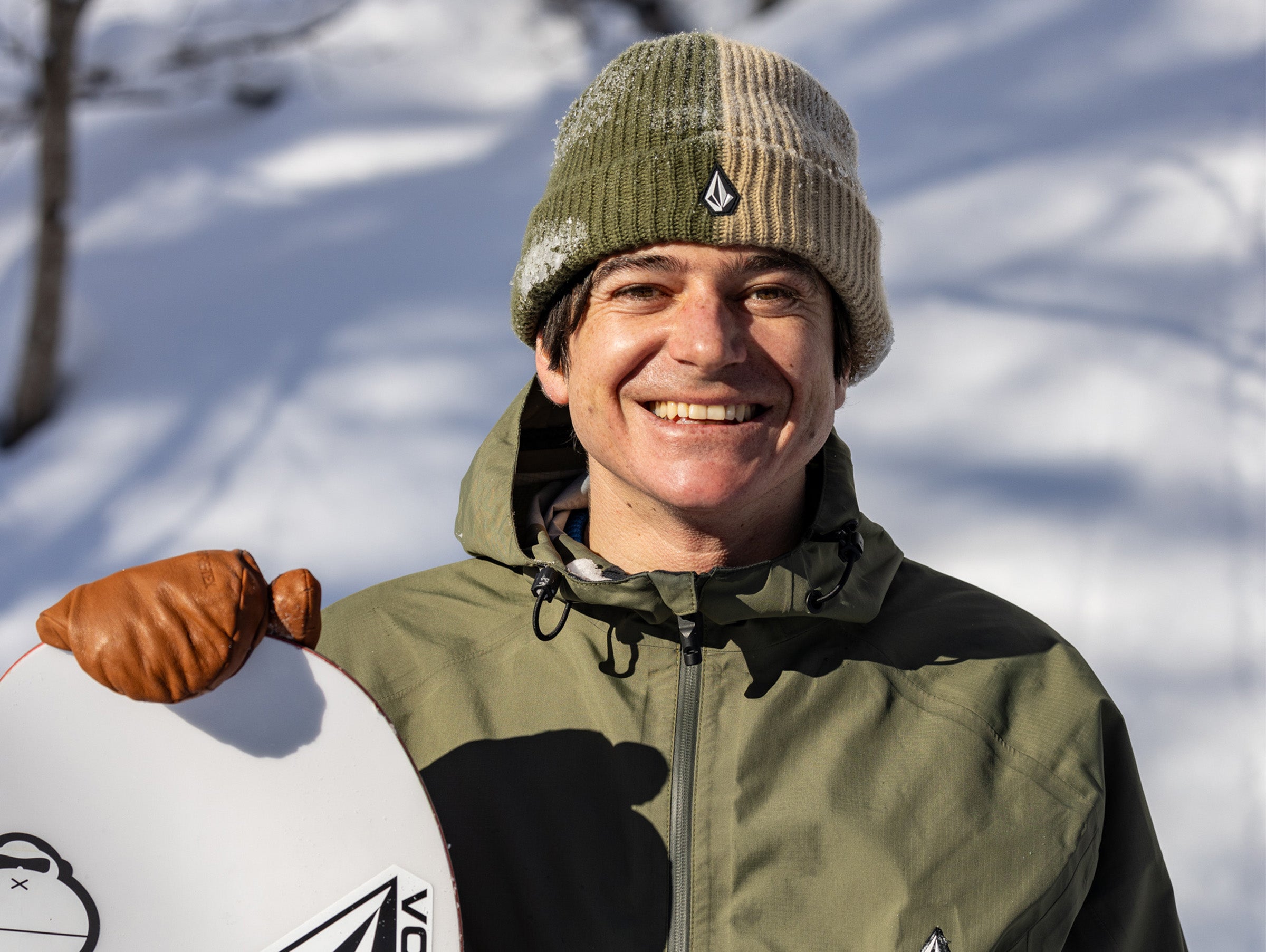 Man in winter clothing holding a snowboard with a snowy background