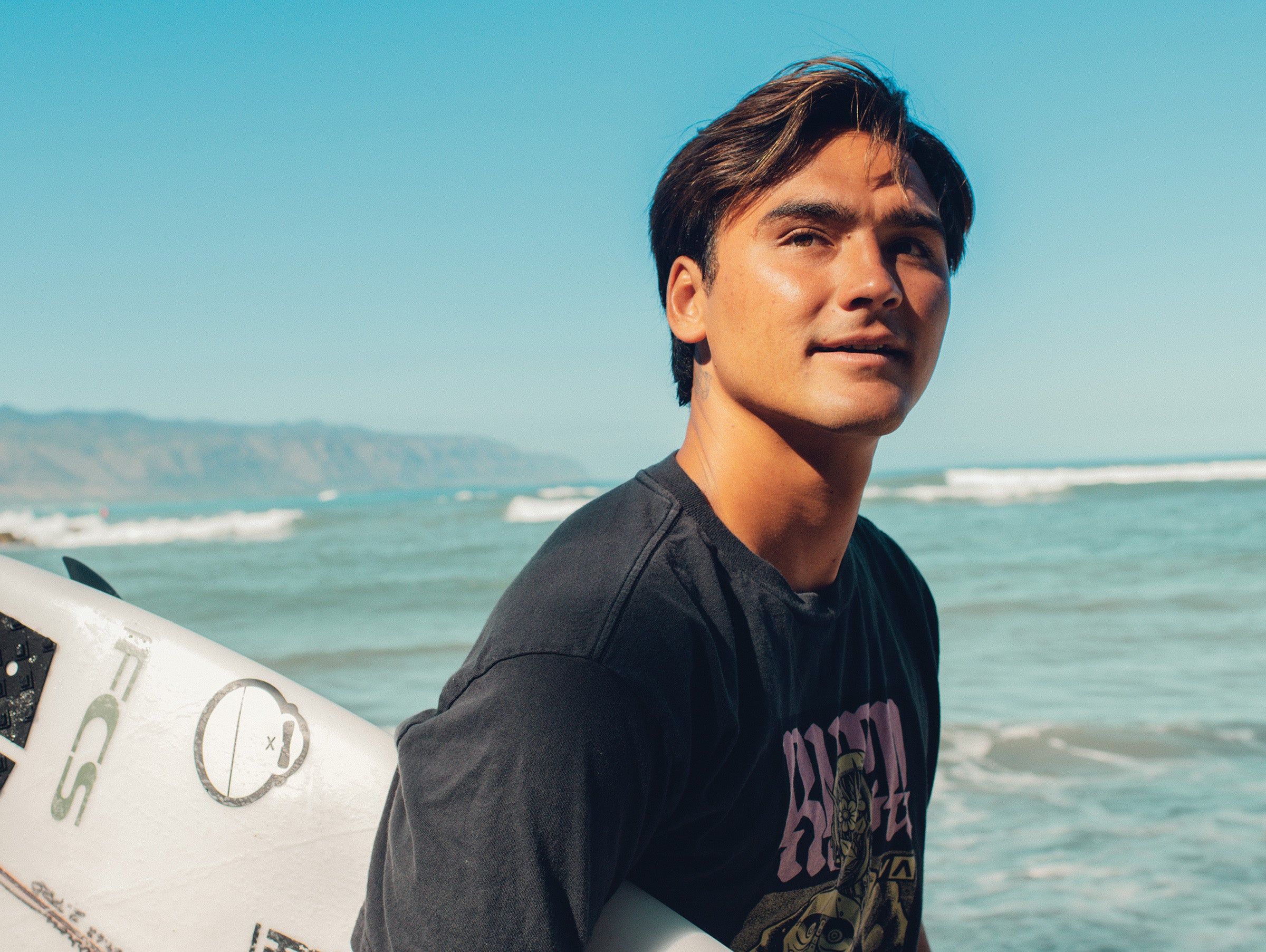 Person holding a surfboard with a beach and ocean in the background