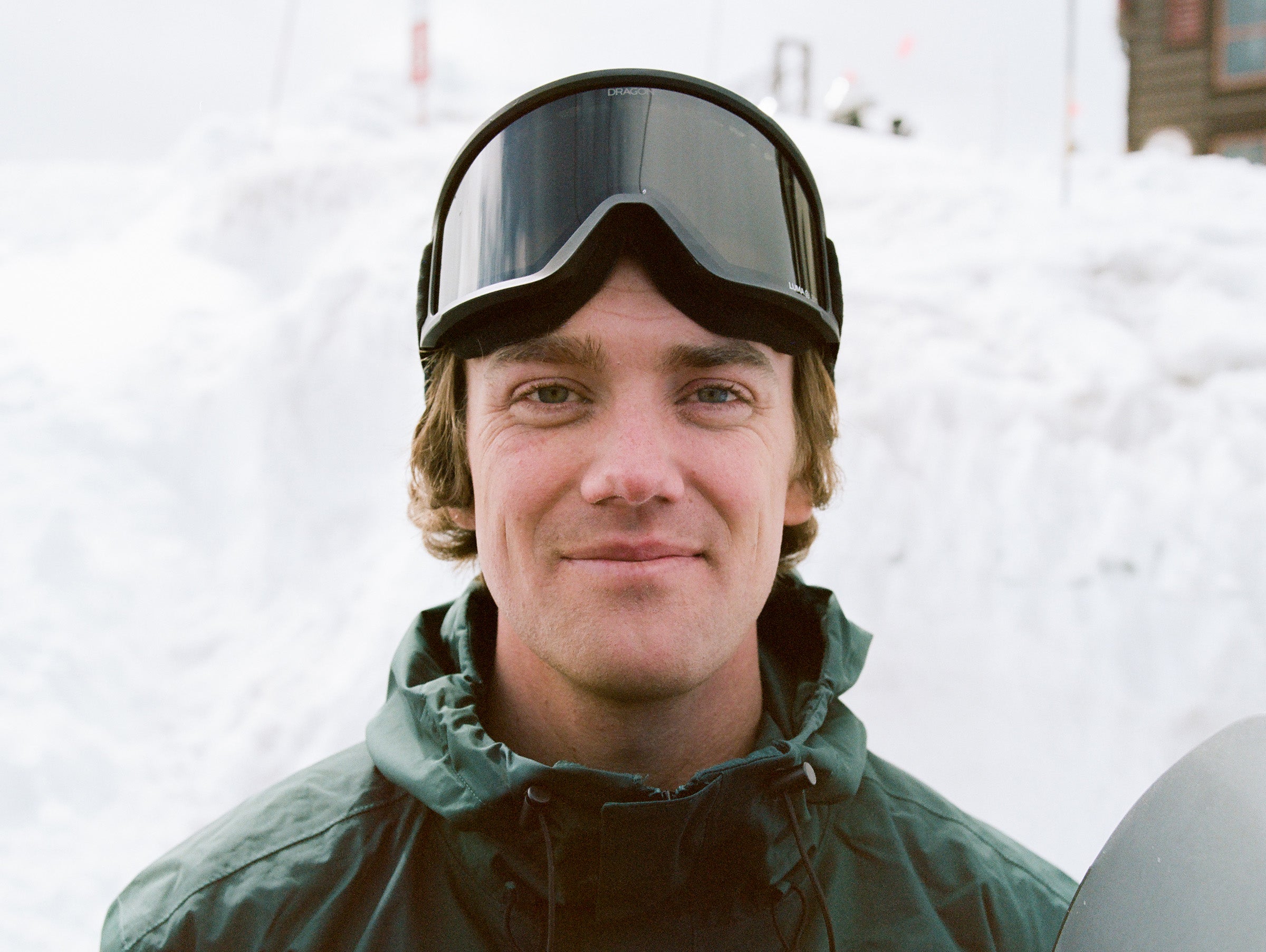 Person wearing ski goggles and a green jacket in a snowy background
