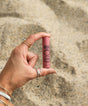 Hand holding a pink lip balm against a textured beige background