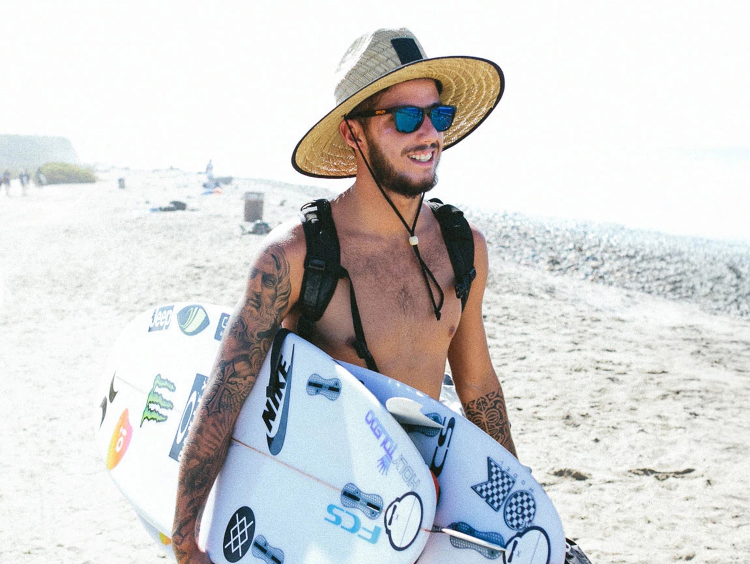 Man with tattoos holding a surfboard on a beach