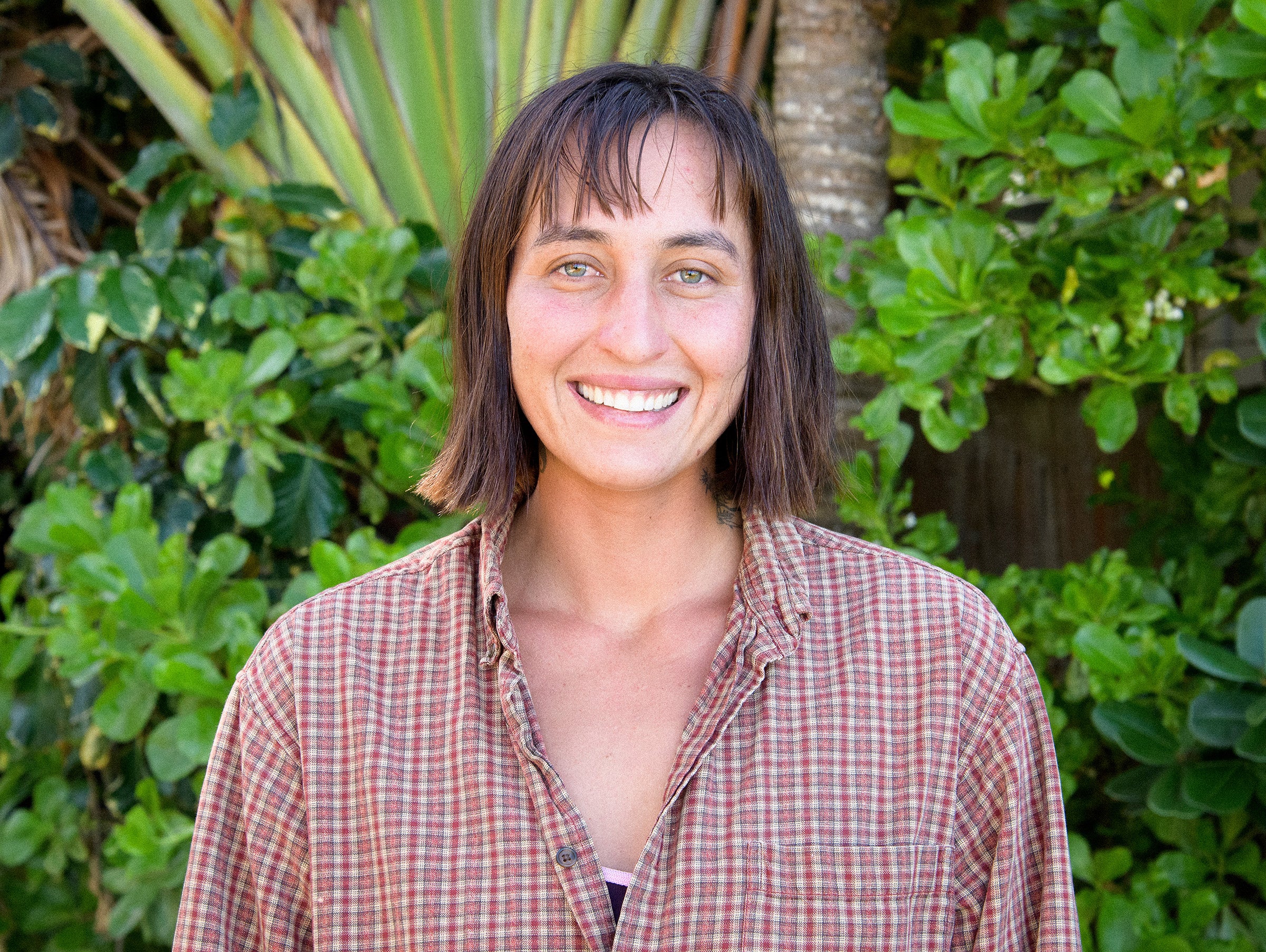 Person wearing a plaid shirt standing in front of green foliage