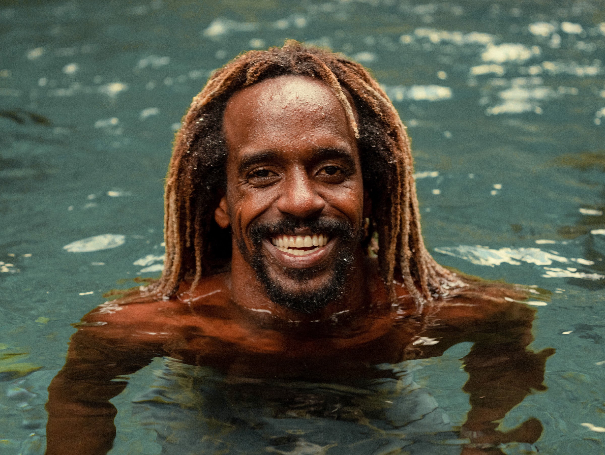 Man with dreadlocks smiling while partially submerged in water