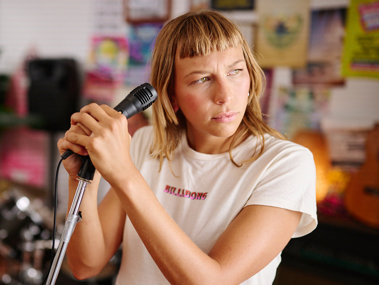 Person holding a microphone in a room with musical instruments and posters on the wall.