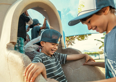 Two children playing together on a playground structure with a clear sky in the background.