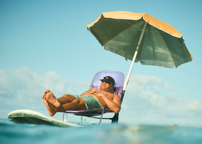 Man relaxing on a beach chair under an umbrella with clear blue sky and ocean.