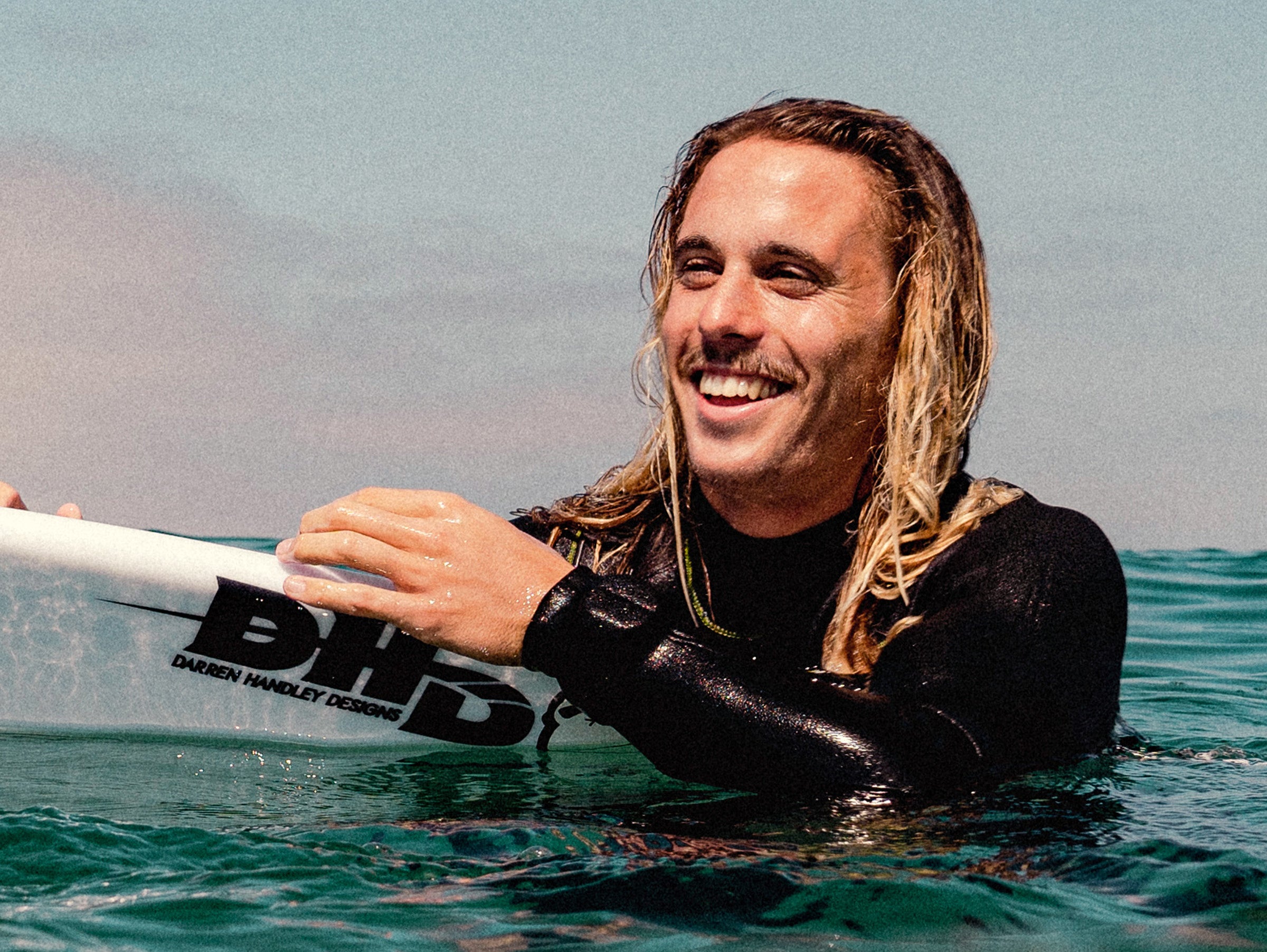 Man in a wetsuit holding a paddle in the water with a clear sky background