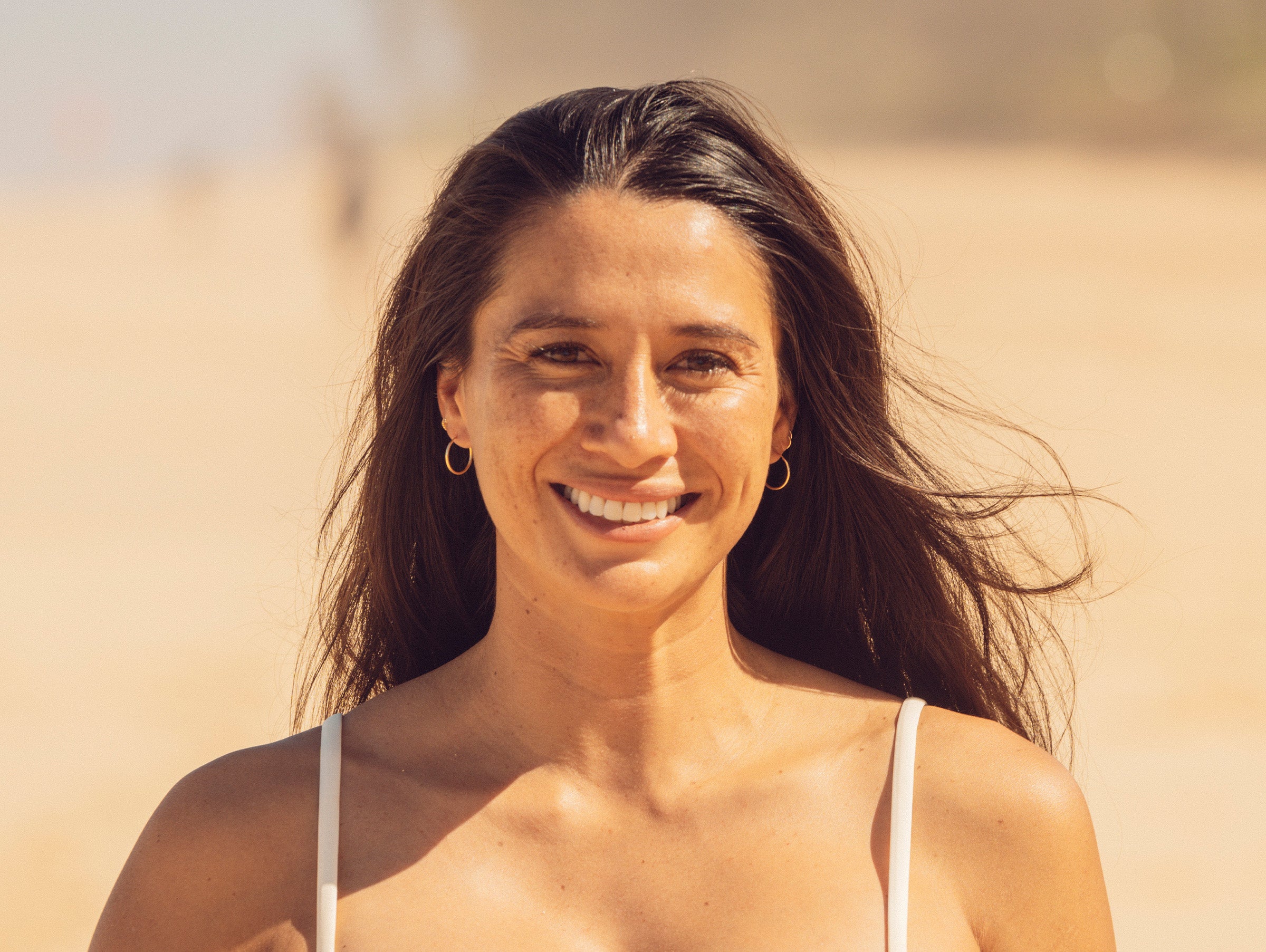 Woman with long dark hair smiling outdoors with a blurred natural background