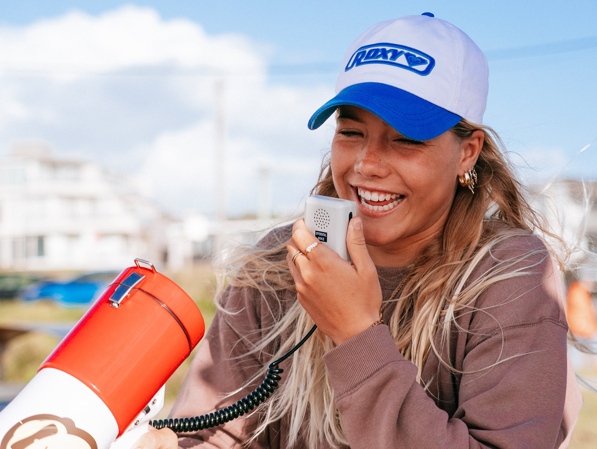 Person wearing a cap with a logo, holding a microphone and megaphone outdoors.