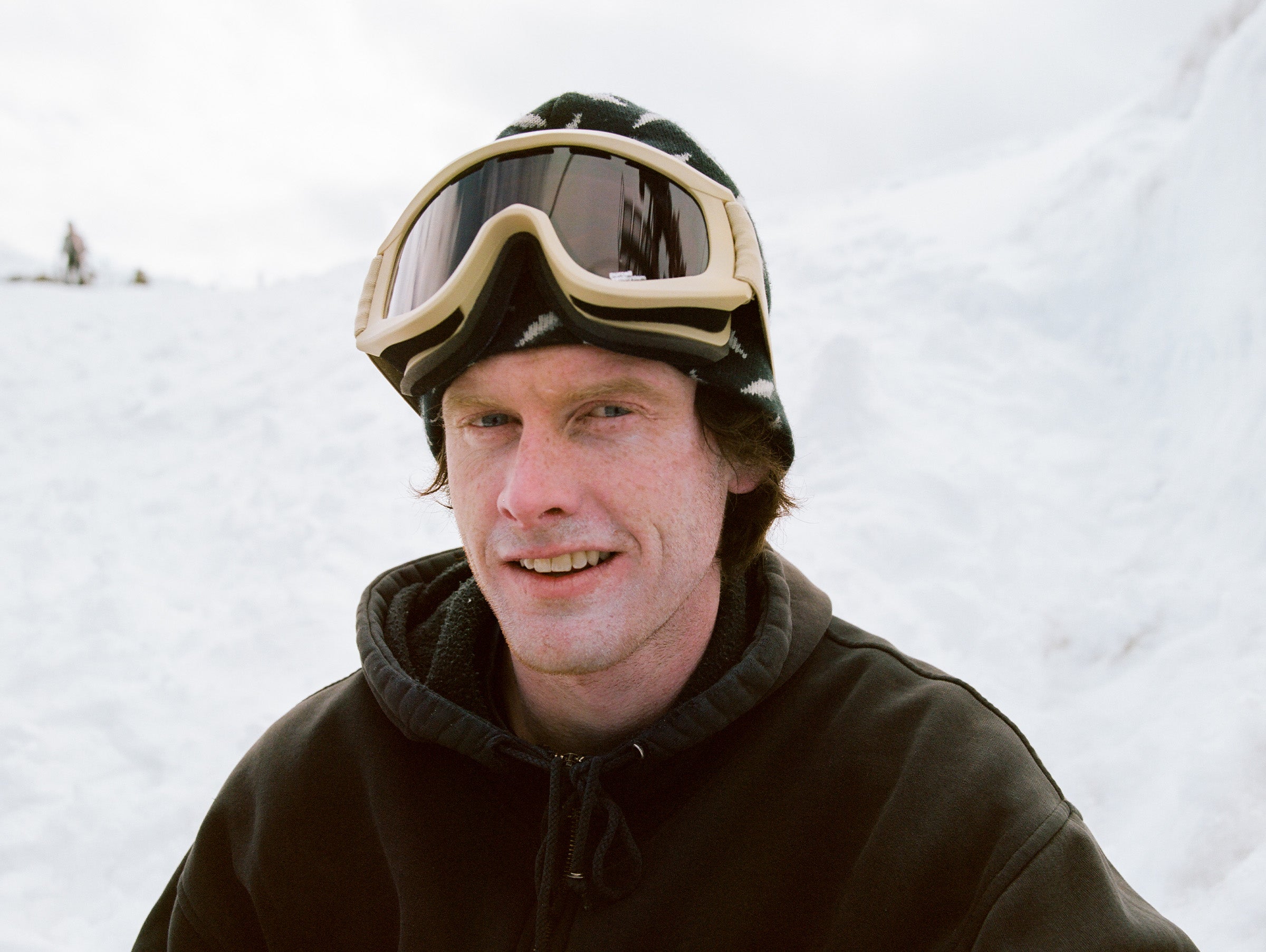 Person wearing ski goggles and a dark jacket in a snowy landscape