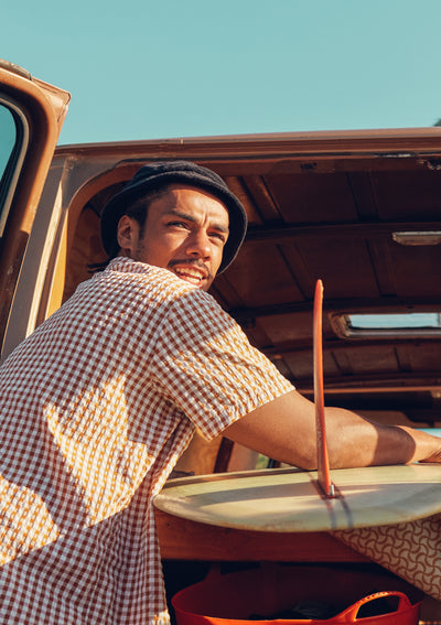 Man sitting in an open car with a checkered shirt and a hat, holding a pot.
