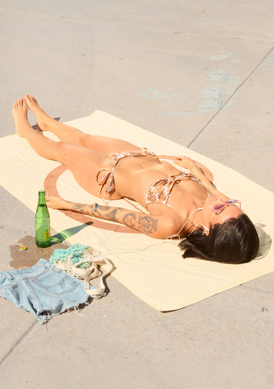 Person lying on a towel with a bottle and shorts nearby on a concrete surface
