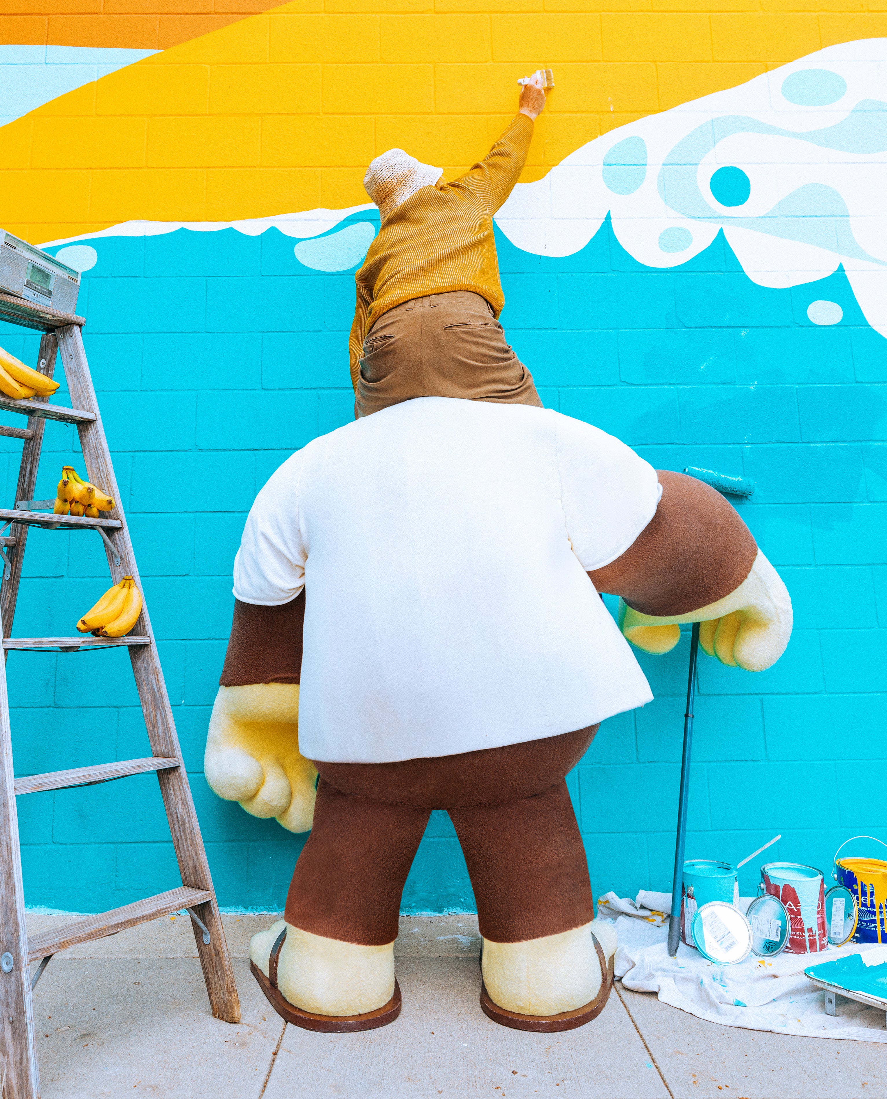 Person in a bear costume painting a colorful mural on a wall.