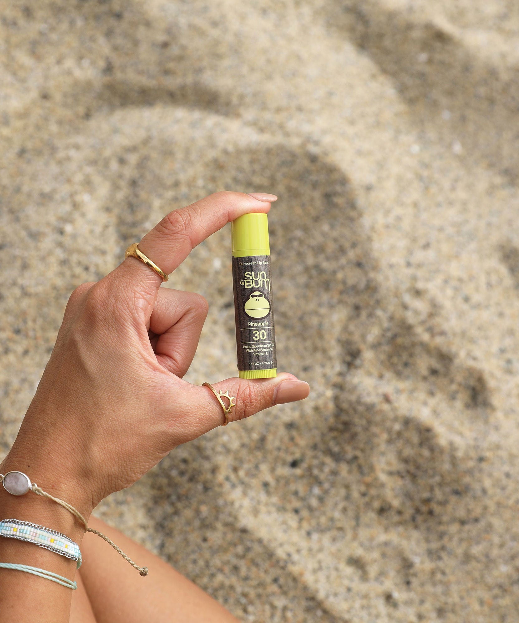 Hand holding a Sun Bum sunscreen stick against a sandy background