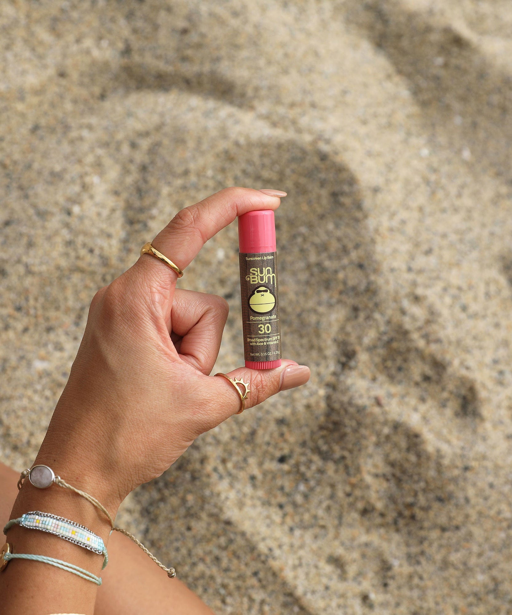 Hand holding a Sun Bum sunscreen stick against a sandy background