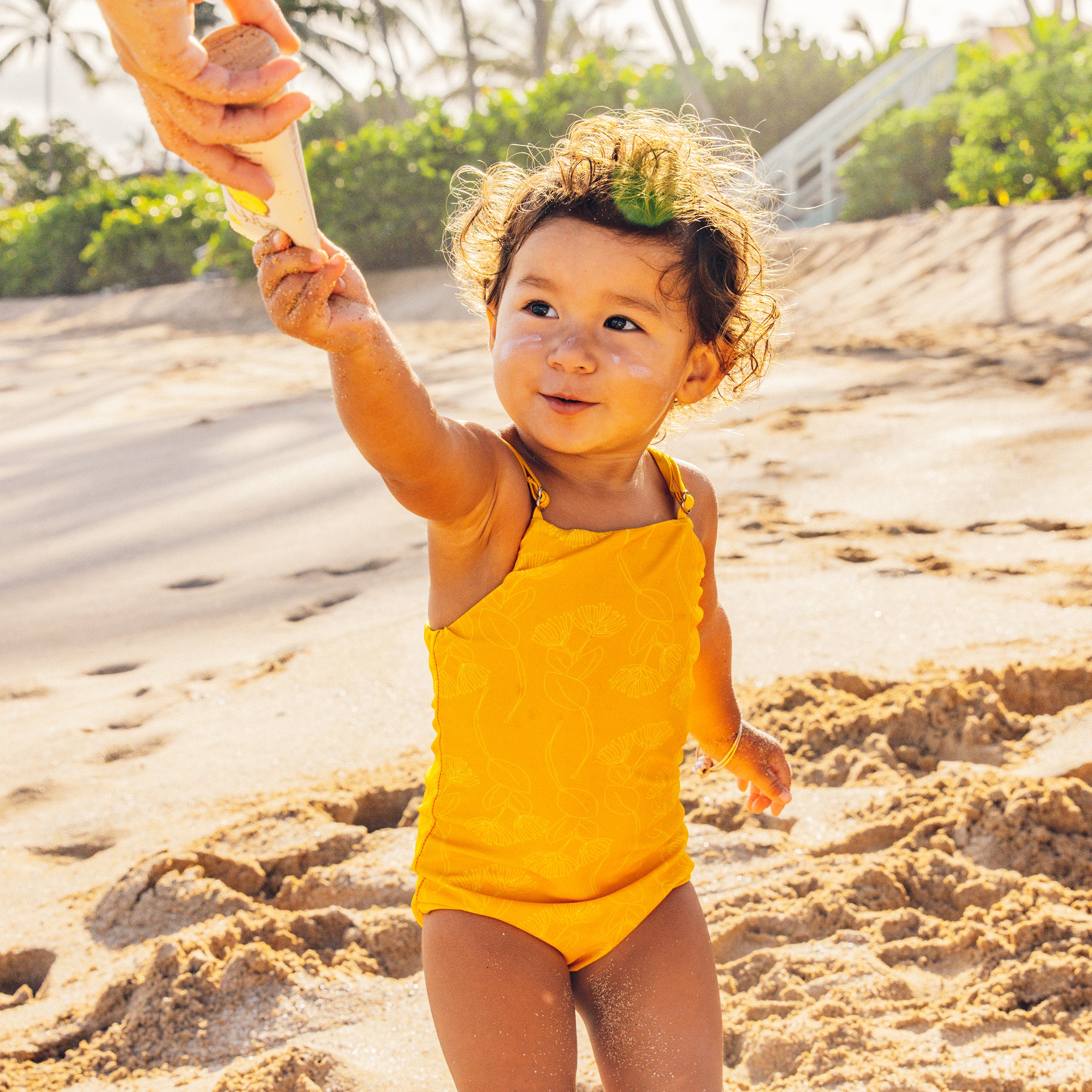 Child in a yellow swimsuit playing on a sandy beach with a shovel.