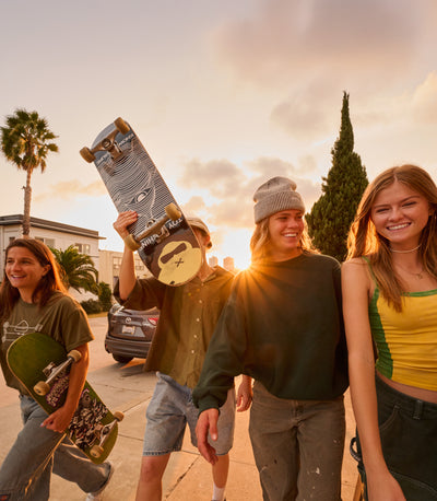 Four friends with skateboards standing outdoors during sunset.